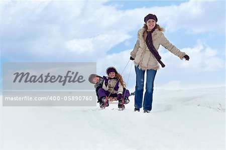 Children having fun on a sleigh in the snow with their mother