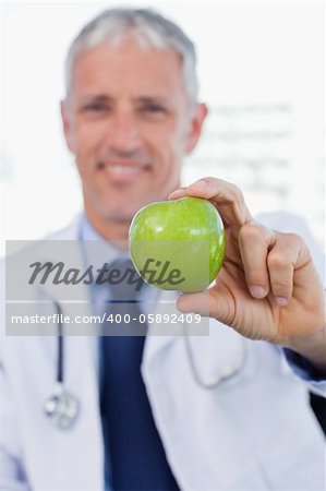 Portrait of a doctor showing an apple in his office