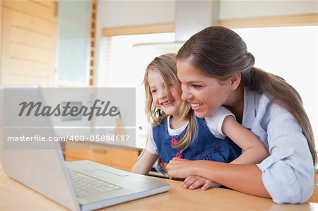Smiling mother and her daughter using a laptop in their kitchen