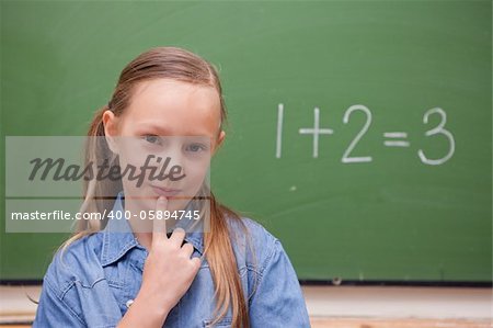 Smiling schoolgirl thinking in front of a blackboard