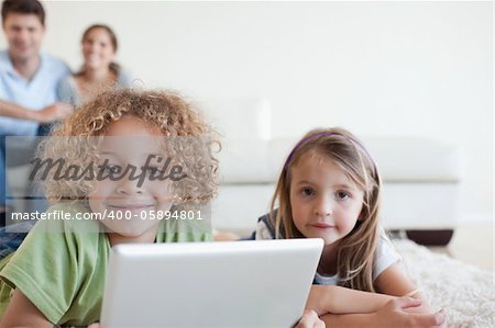 Smiling children using a tablet computer while their happy parents are watching in their living room