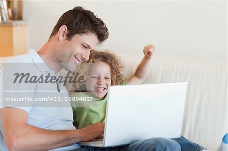 Cheerful boy and his father using a laptop in their living room