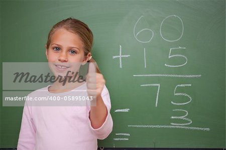 Cute schoolgirl with the thumb up in front of a blackboard