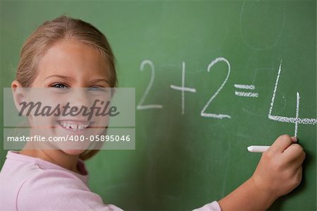 Happy schoolgirl writing a number on a blackboard