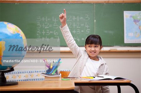 Smiling schoolgirl raising her hand to answer a question in a classroom