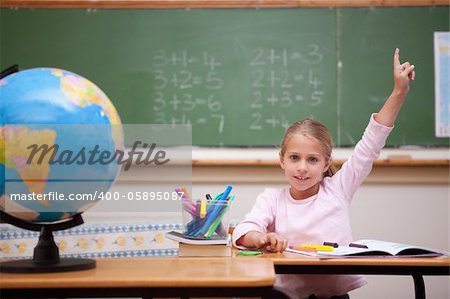 Cute schoolgirl raising her hand to answer a question in a classroom