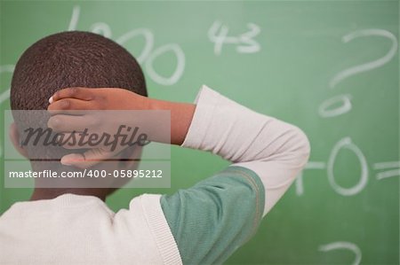 Schoolboy thinking with his hand on his head in front of a blackboard