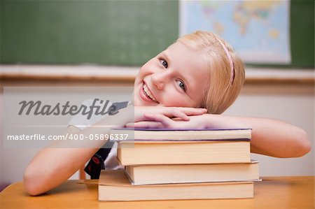 Smiling girl leaning on books in a classroom