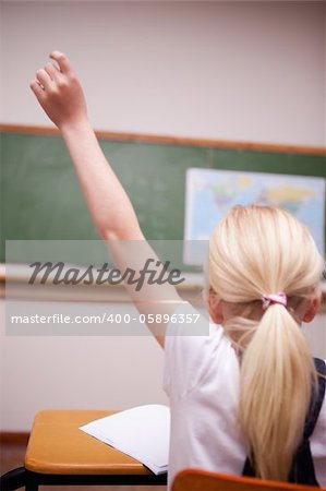 back view of a schoolgirl raising her hand in a classroom