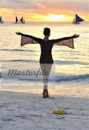Girl on a beach at sunset with outstretched arms