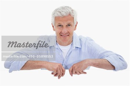 Portrait of a smiling mature man standing behind blank panel against a white background