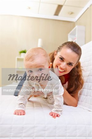 Happy mother and interested baby playing on divan