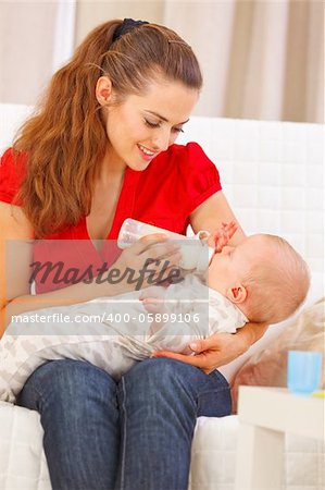Happy mother sitting on sofa and feeding baby