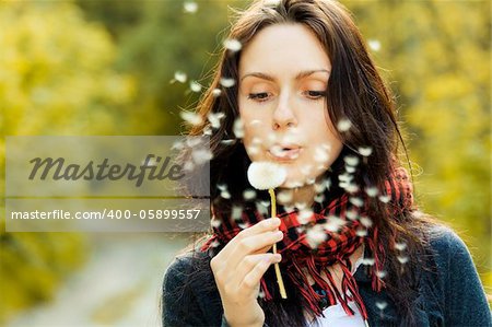 Girl blowing on white dandelion in the forest