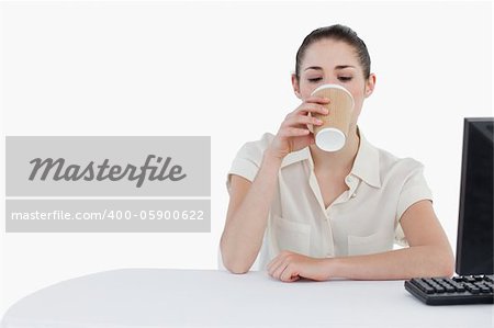 Businesswoman drinking a takeaway tea while using a computer against a white background