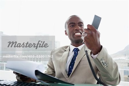 Angry businessman looking at his phone handset in his office
