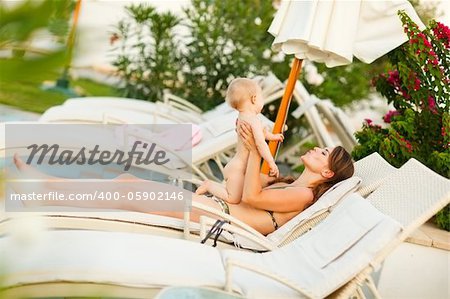 Young mother laying on sunbed and playing with baby