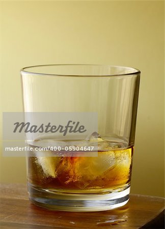 glass of scotch whiskey and ice on gold  background