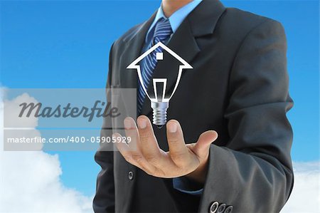 businessman hand holding a light bulb model of a house on sky