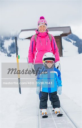 In ski school. Little cute boy in ski goggles and a helmet with his mother on the skier lift