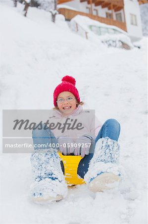 Cute pretty girl in red hat riding on a sled near the Austrian cottage