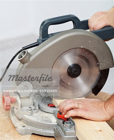 Worker hands cutting wooden plank with electric circular saw - closeup