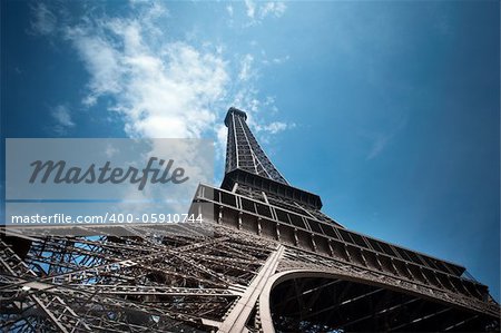 Eiffel Tower in Paris shot from Champs de Mars against a blue sky shoto from unusual angle. Useful file for your brochure, flyer and website about french culture and architecture.