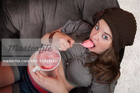 Pregnant woman in cap on sofa eats ice cream