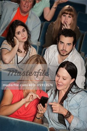 Two women talking in theater with annoyed audience