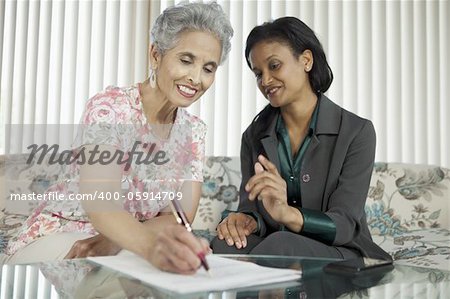 Mature Black woman signing documents at a home meeting with her agent