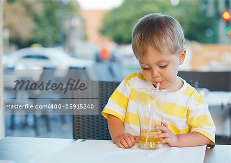 Casual portrait of adorable little boy drinking juice in outdoor restaurant