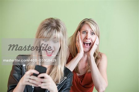 Excited daughter texting with shocked mom behind her over green background