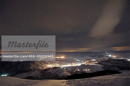 Small night town in the mountains under cloudy starry dark sky