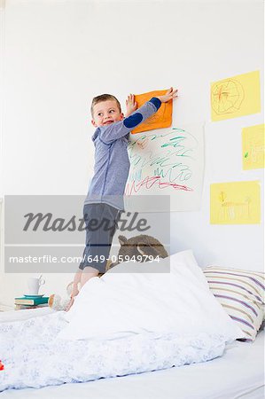 Boy hanging drawing on bedroom wall