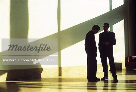 Businessmen talking in shadowed lobby