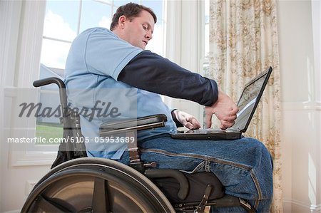 Mann mit Querschnittslähmung im Rollstuhl auf einem Laptop mit seinen behinderten Händen arbeiten