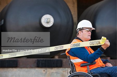 Facilities engineer in a wheelchair pulling caution tape in front of chemical storage tanks