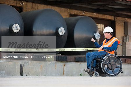 Ingénieur des installations en fauteuil roulant en tirant la bande de protection devant les réservoirs de stockage de produits chimiques Ingénieur des installations en fauteuil roulant en tirant la bande de protection devant les réservoirs de stockage de produits chimiques