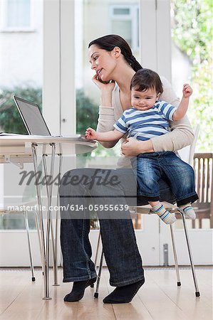 Mère tenant le petit garçon, à l'aide de téléphone portable et ordinateur portable