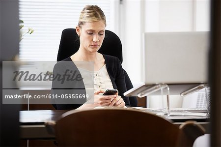 Businesswoman at desk, looking at cellphone