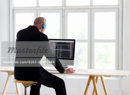Businessman listening to headphones, using computer in office