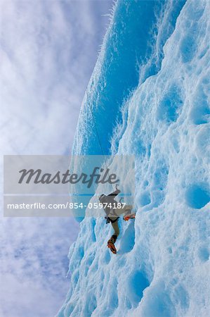 An ice climber ascends the face of a large iceberg frozen into Mendenhall Lake, Juneau, Southeast Alaska, Winter