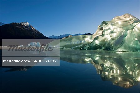 An iceberg, trapped in the frozen waters of Mendenhall Lake glowing and backlit with the morning sun, Juneau, Southeast Alaska, Winter