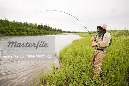 Fly fisherman wearing mosquito protection fishes for salmon on the Mulchatna River in the Bristol Bay area, Southwest Alaska, Summer