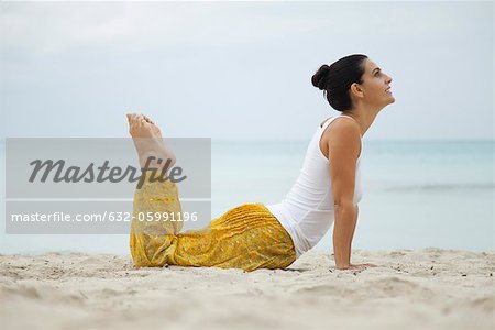Mature woman practicing yoga on beach, side view