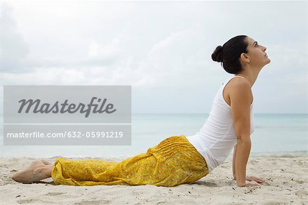Mature woman in cobra pose on beach, side view