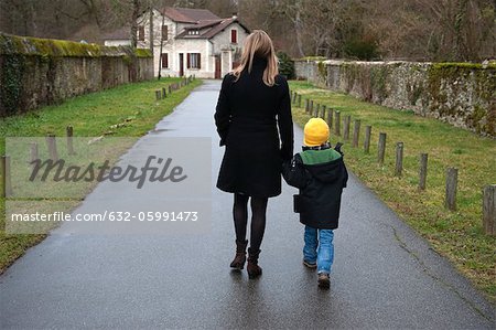 Mère et son fils marcher sur le chemin d'accès au village, main dans la main, vue arrière