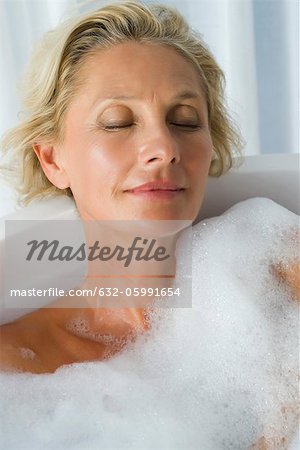 Femme mature se détendre dans le bain à bulles avec les yeux fermés, portrait