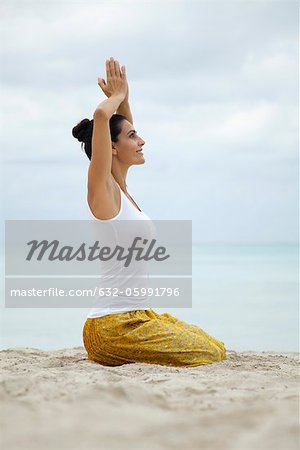 Mature woman kneeling in prayer position with hands above head, side view