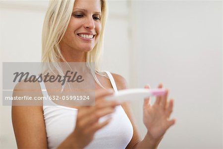 Mid-adult woman looking at pregnancy test with cheerful expression